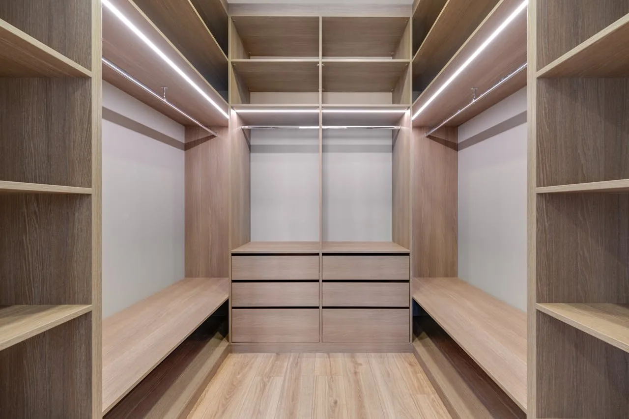 Spacious walk-in closet with wooden shelves and LED lighting creates a minimalist and modern design.
